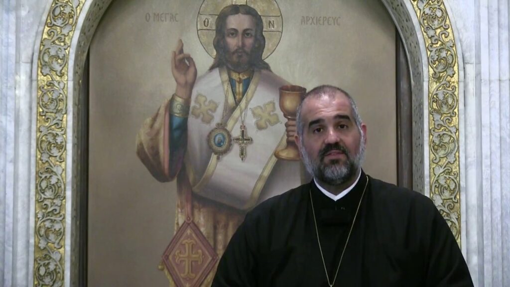 Priest standing before religious icon painting.