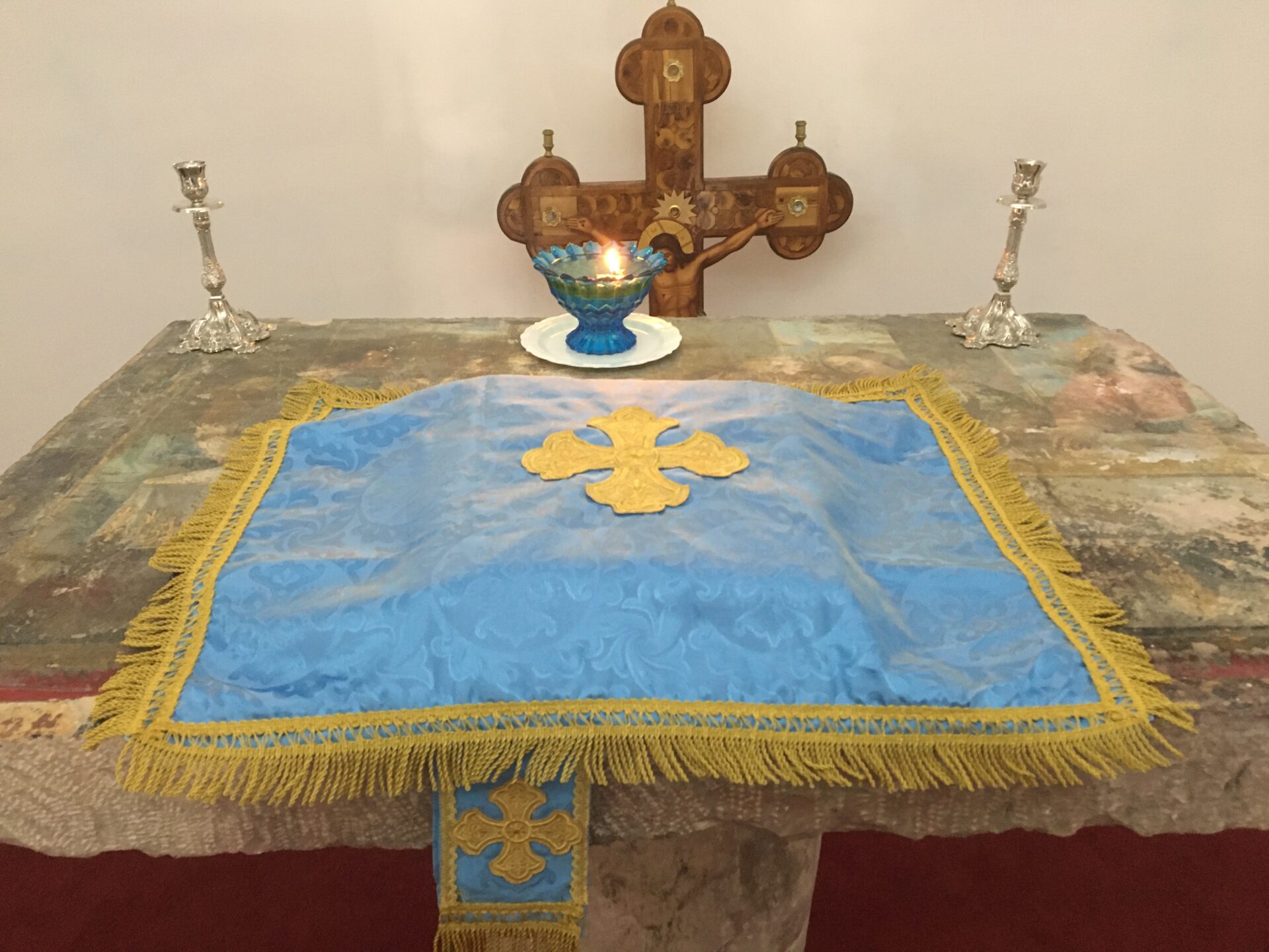 Altar with cross, candle, and blue cloth.