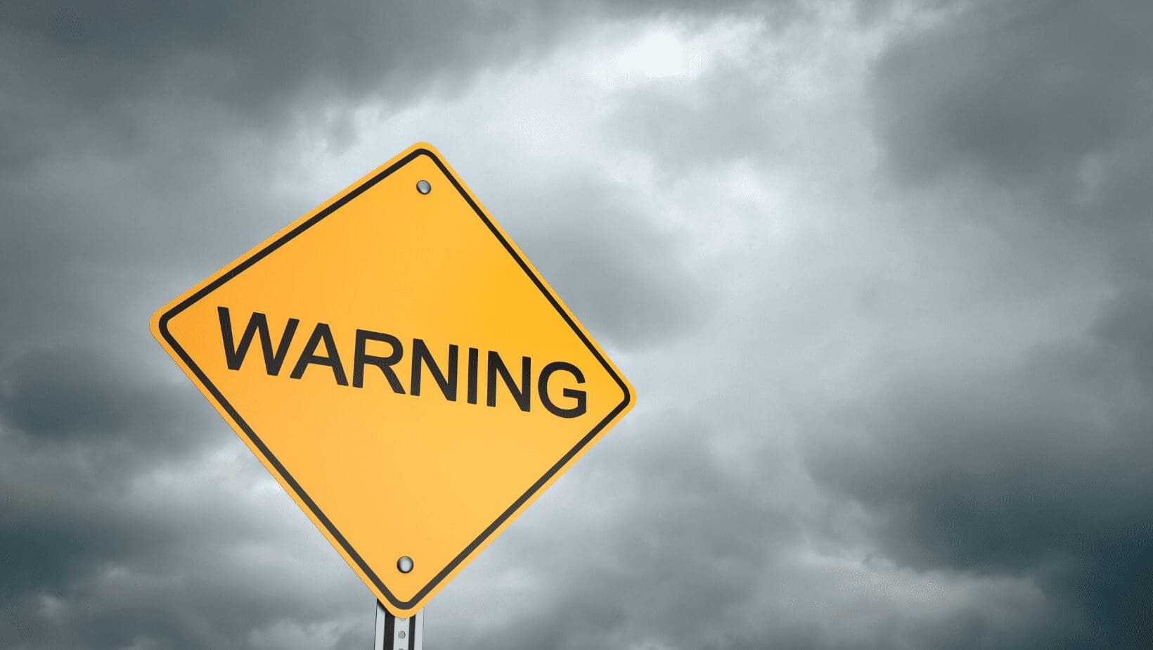 Yellow warning sign against cloudy sky.