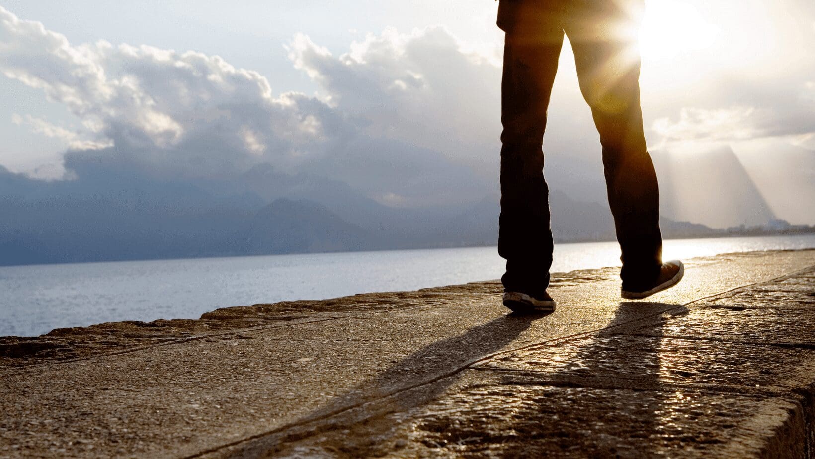 Person standing by water at sunrise.