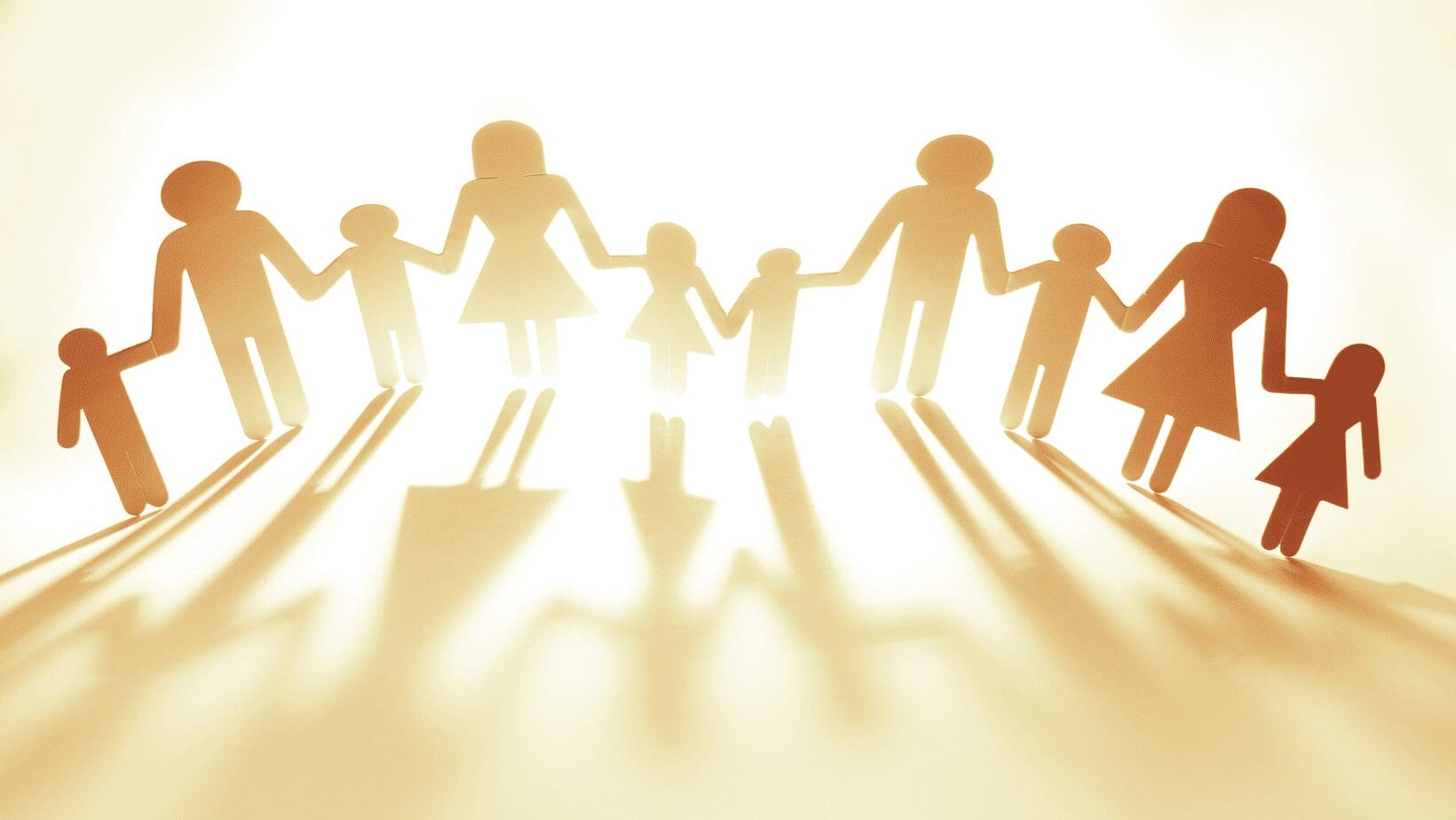 Paper cut-out family holding hands casting shadows on a sunlit surface.