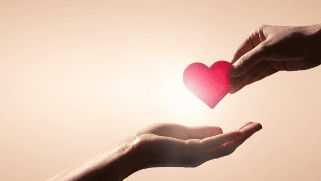 Hands exchanging a red heart symbol.
