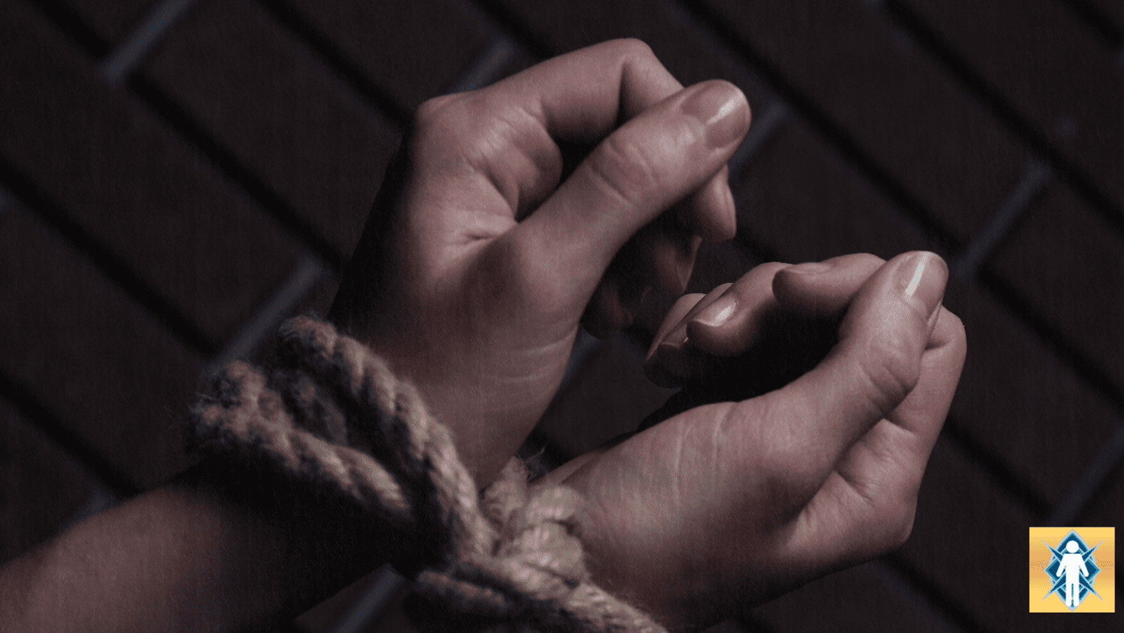 Hands tied with rope against brick background.