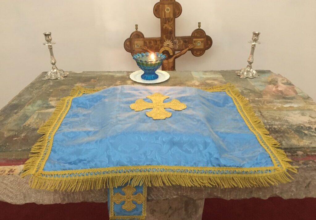 Altar with cross, candle, and blue cloth.