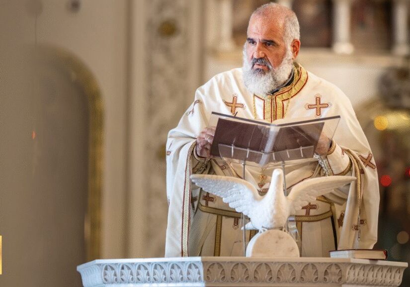 A priest holding a book with a dove flying near a baptismal font.