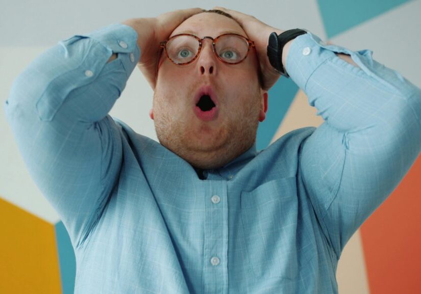 Surprised man expressing shock with hands raised.