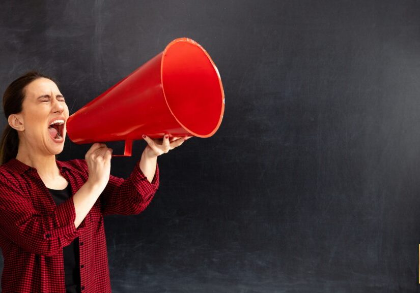 Person using a large red megaphone against a black background.