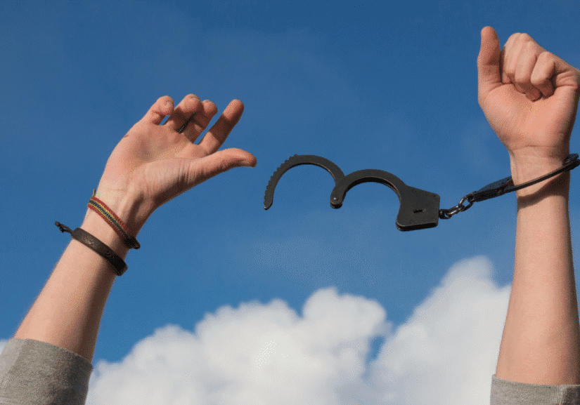 Hands breaking free from handcuffs against sky.