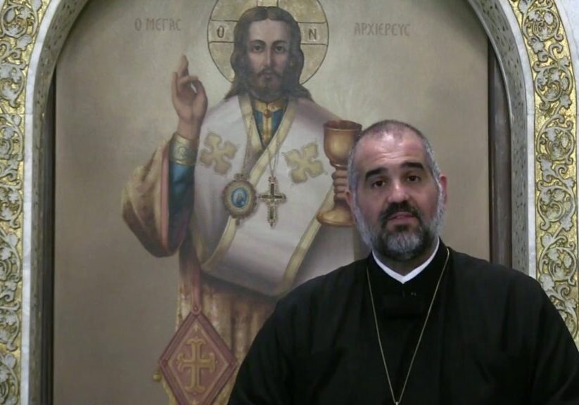 Priest standing before religious icon painting.